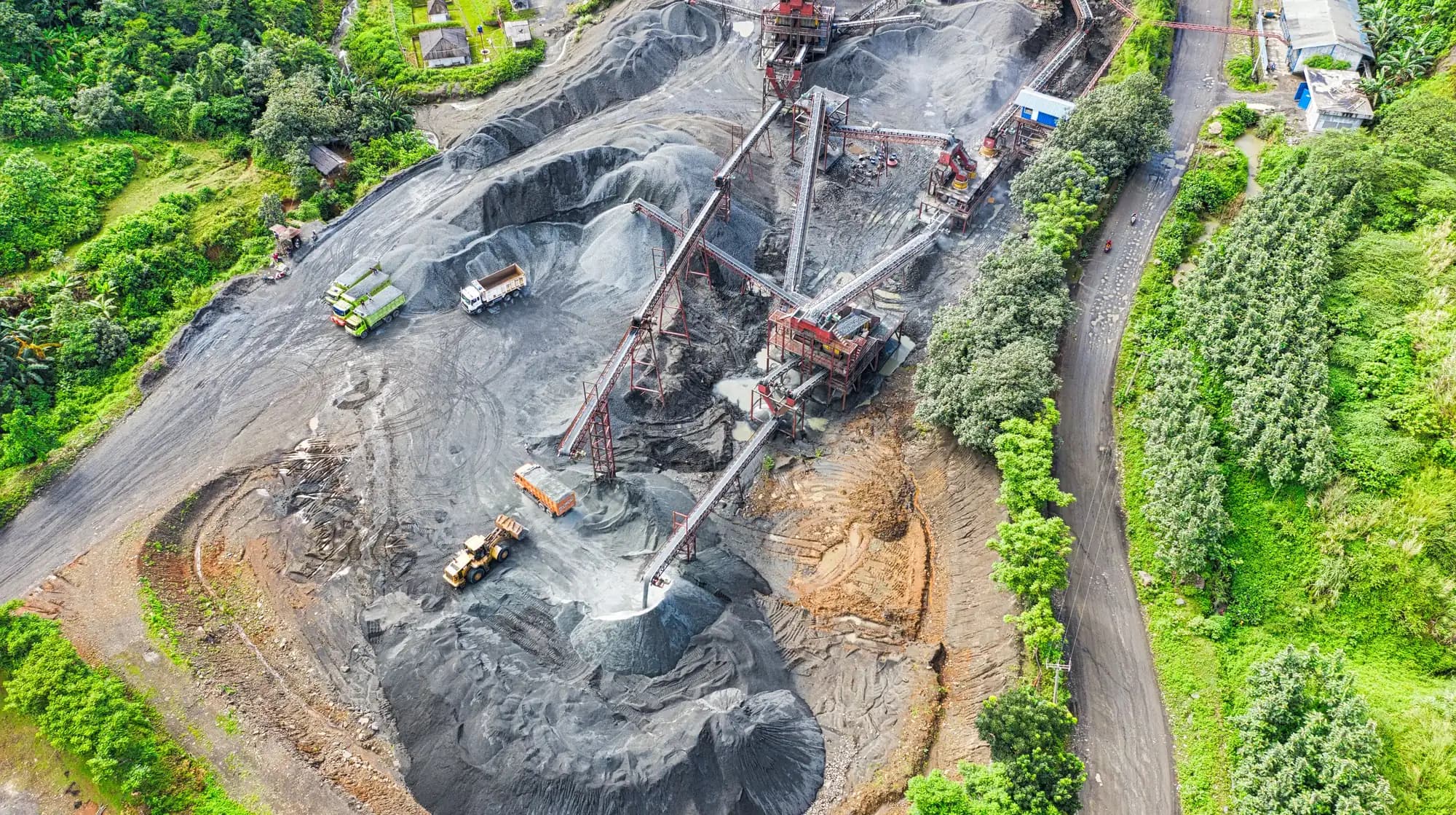 A quarry processing plant with conveyors and haul trucks, seen from the air